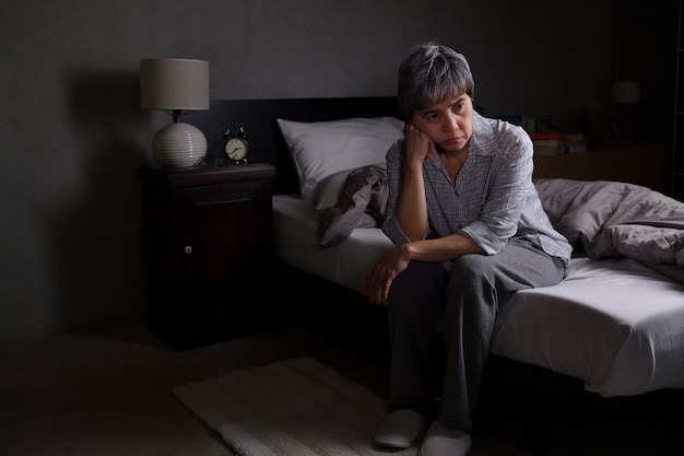 Depressed senior woman sitting in bed cannot sleep from insomnia