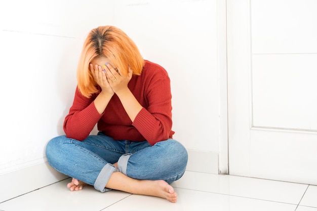 Depressed teenager sitting with crossed legs in the corner with hands covering her face