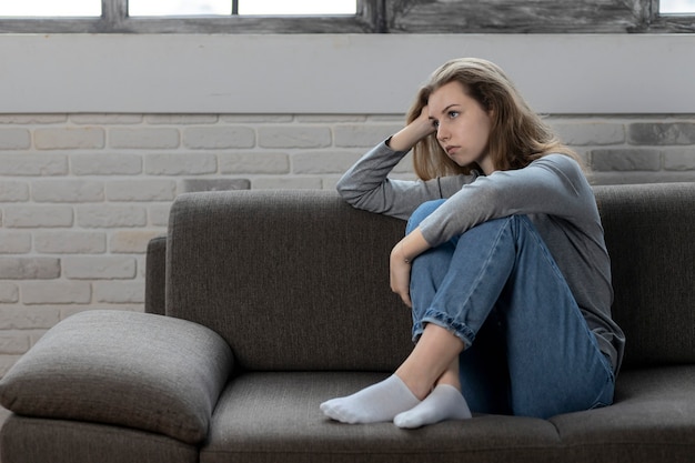 Depressed teenager with sad emotions and feelings sitting on the couch at home