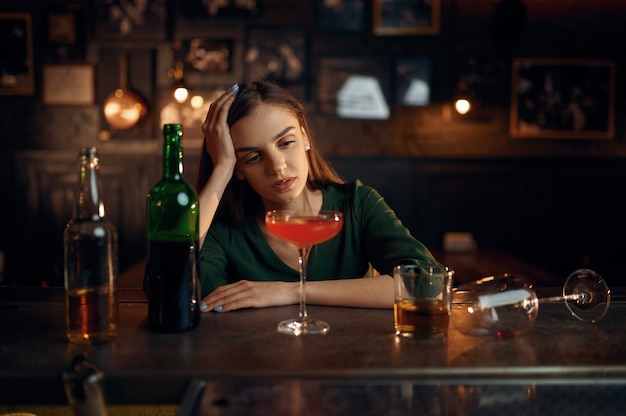 Подавленная женщина пьет разный алкоголь за стойкой в баре