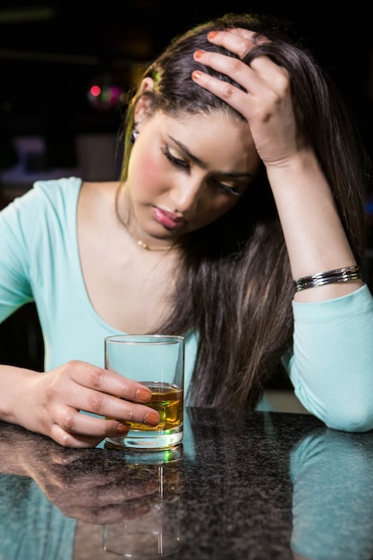 Donna depressa che mangia whiskey al contatore della barra nella barra