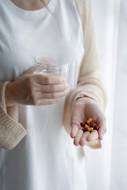 Depressed woman holding a glass of water suffering from headaches fighting stress with antidepressants closeup view