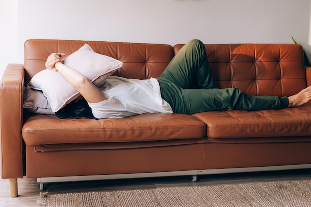 Photo depressed woman lies on the couch and covers her face with a pillow