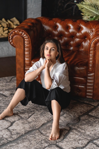 Depressed woman sitting on the floor near the armchair at home