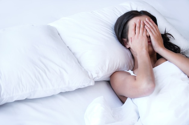 Depressed women in bed. Top view of young sad women lying on the bed and hiding her face in hands