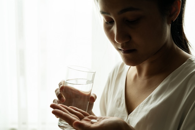 落ち込んでいる女性の手は、コップ1杯の水で薬を保持します