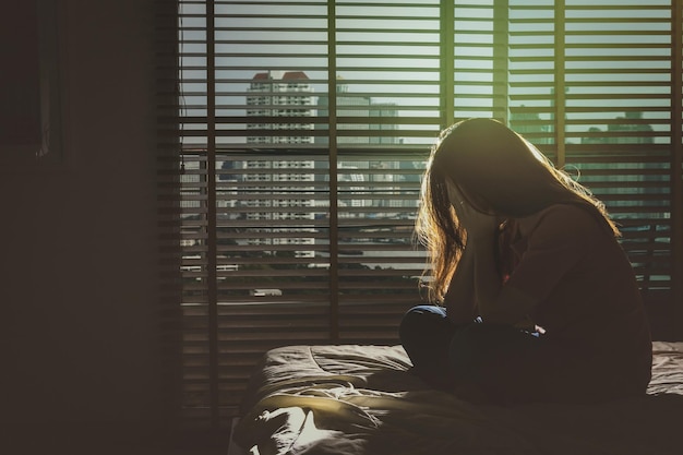 Photo depressed women sitting head in hands on the bed in the dark bedroom with low light