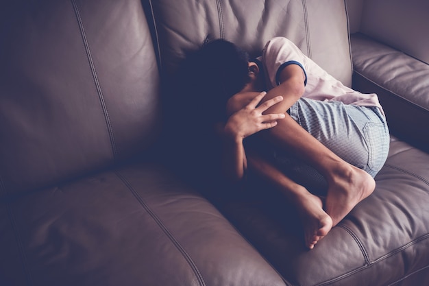 Depressed young boy sitting alone on sofa at home, children mental health