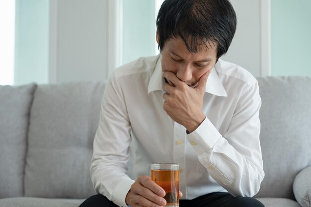 落ち込んだ若いビジネスマン中毒気分が悪い家で一人でウィスキーを飲むストレスを感じたイライラした孤独な飲酒は問題のある酒アルコール依存症に苦しんでいます人生と家族の問題