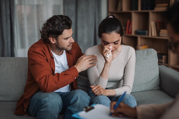 Depressed young european male calm crying female on psychological consultation in clinic