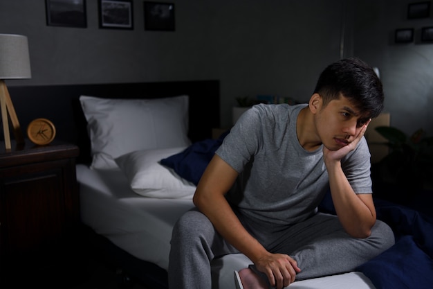 Depressed young man suffering from insomnia sitting in bed

