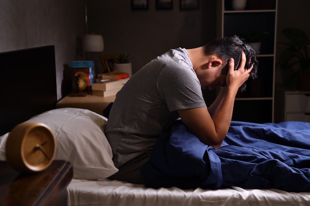 Depressed young man suffering from insomnia sitting in bed

