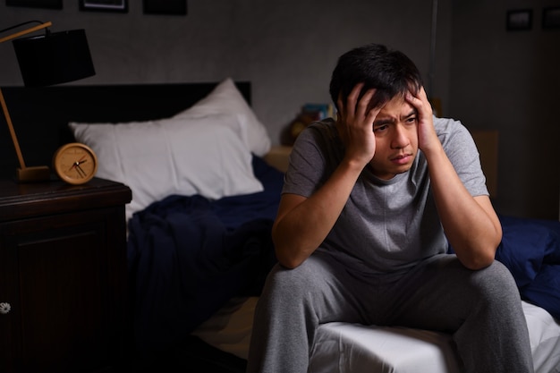 Depressed young man suffering from insomnia sitting in bed

