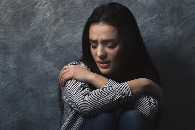 Depressed young woman on grey wall background