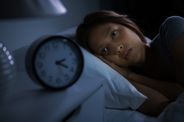 ベッドに横たわっている落ち込んでいる若い女性は不眠症から眠ることができません