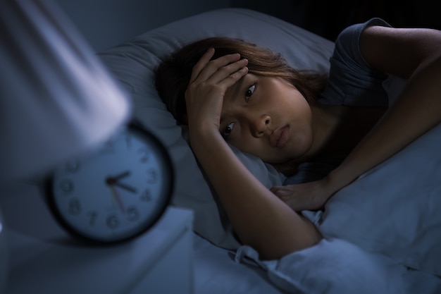 침대에 누워 우울한 젊은 여성이 불면증으로 잠을 잘 수 없습니다