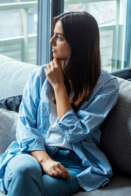 Depressed young woman sitting on couch in the living room at home Frustrated confused female feels unhappy problem in personal life quarrel break up with boyfriend