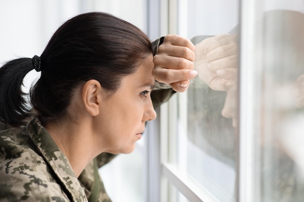 Depressie concept peinzende vrouw in militair uniform kijkt uit het raam