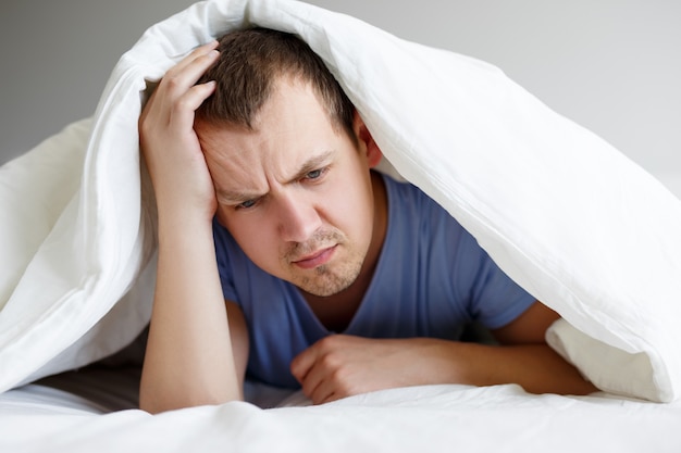 Depressie concept - verdrietig of vermoeide man liggend in bed onder deken