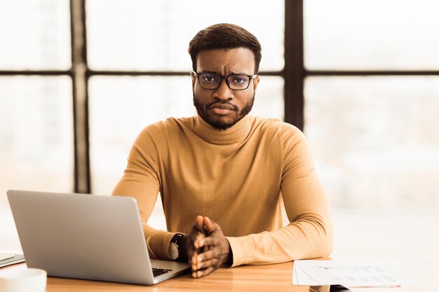 Depressieve afro-manager kijkt naar de camera op het werk.