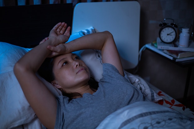 Foto depressieve aziatische vrouw kan niet slapen op het bed. slapeloosheidssyndroom slapeloos na ongelukkig en zorgen maken over haar levensstijl. volwassene voelt verdriet. slechte emotie.