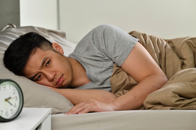 Depressieve jonge Aziatische man die in bed ligt kan niet slapen van slapeloosheid