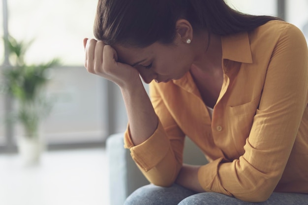 Depressieve jonge vrouw die thuis in de woonkamer zit, voelt zich hopeloos en verdrietig