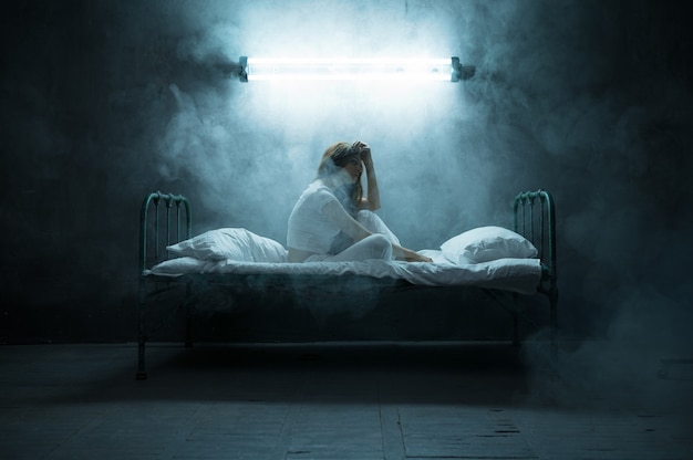 Depressieve psycho vrouw zittend in bed, slapeloosheid, donkere kamer ... Psychedelische vrouwelijke persoon die elke nacht problemen heeft, depressie en stress, verdriet, psychiatrie ziekenhuis