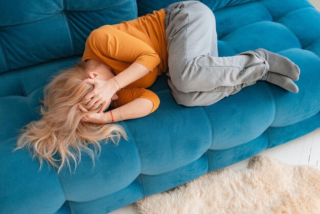 Depressieve volwassen vrouw liggend op de bank met haar armen om zich heen die haar hoofd bedekt met handen ongelukkige vrouw die lijdt aan slapeloosheid depressie psychologisch probleem