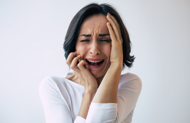 Depressieve vrouw met kort kapsel die huilt terwijl ze haar gezicht aanraakt. Meisje dat schreeuwt met haar ogen dicht vanwege haar psychische aandoening.