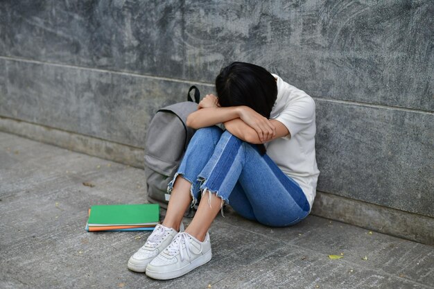 Depressieve vrouw zit op het voetpad tegen een grijze muur.