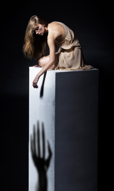 Depressieve vrouw zittend op een stenen voetstuk studio opname donkere achtergrond