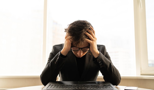 Foto depressieve zakenman met hoofdpijn op kantoor zakelijk directeur met migraine handen op het hoofd van een freelancer op de werkplek