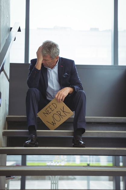 Depressieve zakenman zittend op trap met kartonnen blad met tekst werk nodig