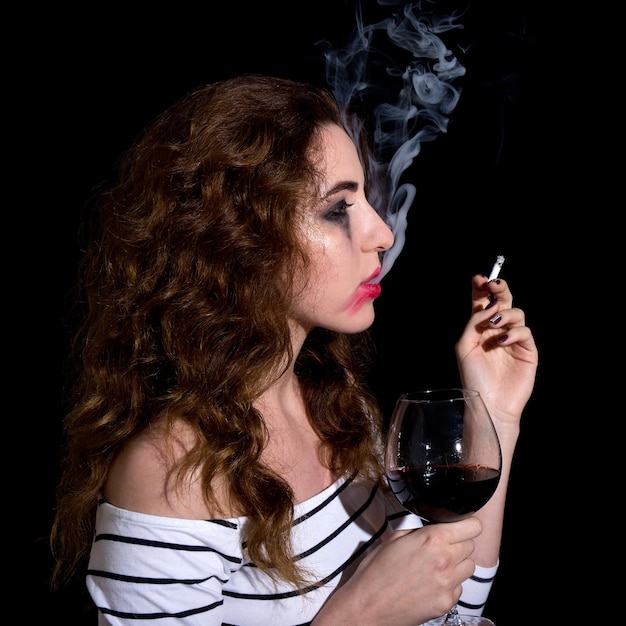 Depression and addiction concept - crying sad woman drinking\
wine and smoking isolated on black background