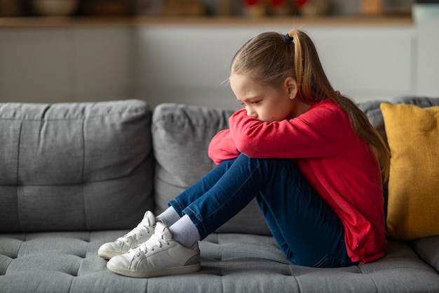 Depression in children upset little girl sitting on couch at home