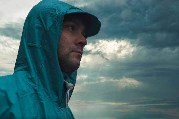 Depressive concept with lonely man in raincoat standing on wet\
road under rain close up