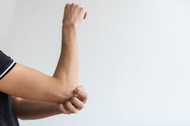 Dermatitis, eczema, allergy, psoriasis concept. man scratching itch on his arm, grey studio background. man itching rash on his elbow, copy space