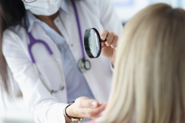 Dermatologist examines patient's face through magnifying glass. Facial skin problems psychosomatics concept