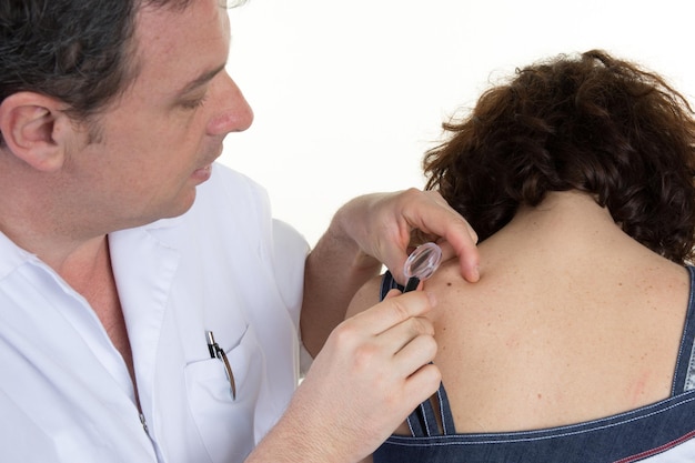 Dermatologist male looking at woman's mole on her back