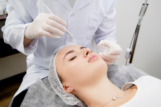 Dermatologist's putting nutrition mask on the young and beautiful woman skin after cleaning to make her skin smooth and healthy.