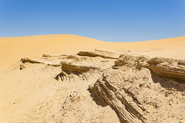 Desert landscape layered sandstone rocks against the background of the dunes