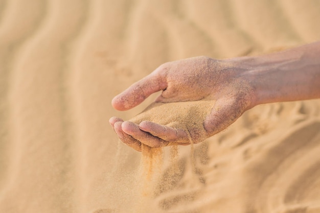 Desert, sand puffs through the fingers of a man's hand.