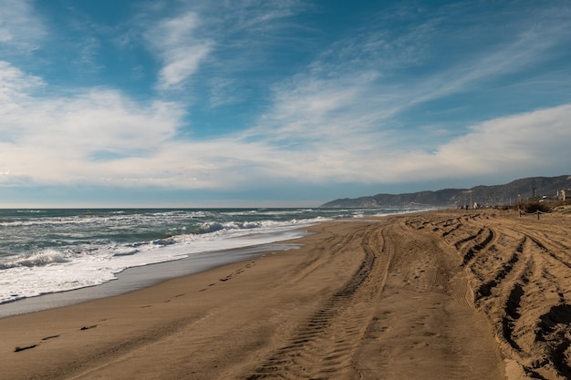 Photo deserted sandy beach with foamy waves and tire tracks under a vast blue sky