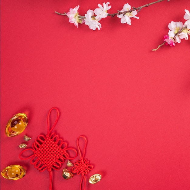 Design concept of chinese lunar new year beautiful chinese knot with plum blossom isolated on red background flat lay top view overhead layout