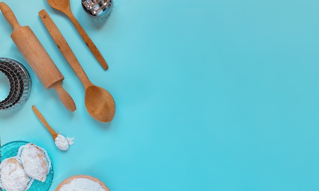 Design concept of making traditional cyprus cookies, baking wooden spoons, rolling pin, metal molds, sugar powder,layout top view, flat lay, overhead, blank copy space on blue background