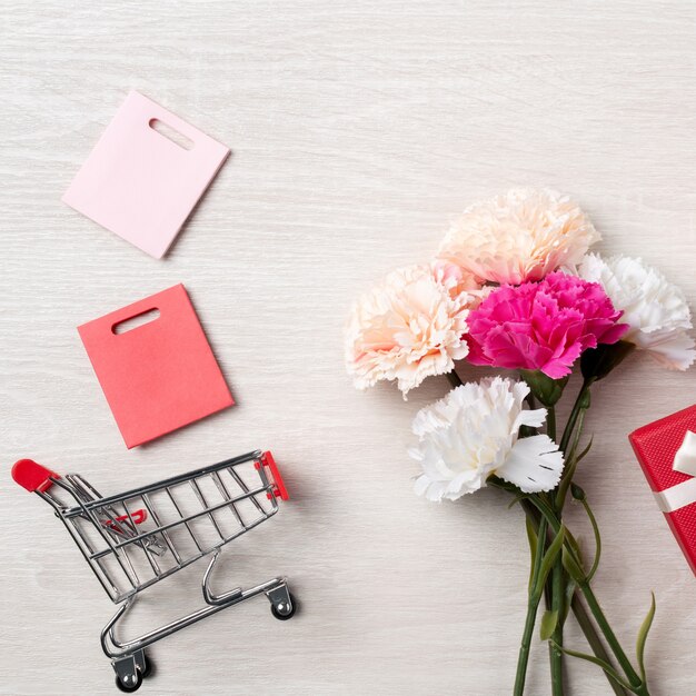 Concetto di design del saluto di festa della mamma con fiore di garofano, idea regalo per le vacanze e carrello su fondo in legno.