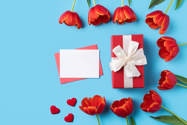 Design concept of Mother's day holiday greeting gift with red tulip bouquet and card on bright blue table background