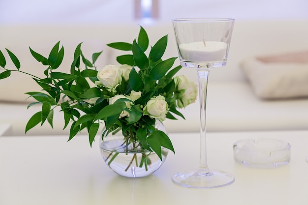 Design and decor decoration of the wedding celebration with white roses, green leaves, candles and bouquets of flowers