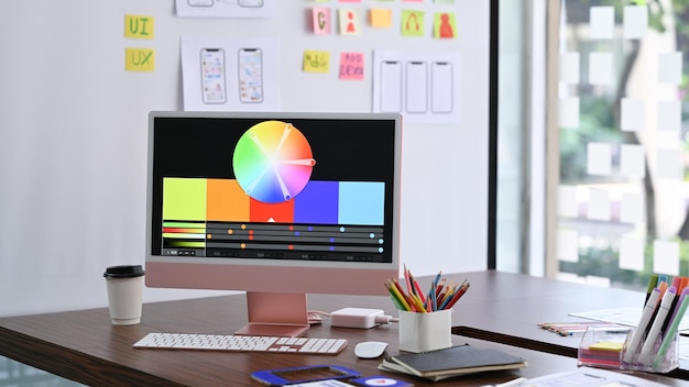 design studio with computer color swatches and wireframe sketches for mobile application on wooden table